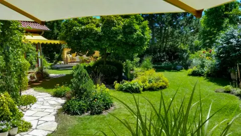 Weiter Blick über einen Garten mit geschwungenem Plattenweg, bunten Staudenbeeten und offener Rasenfläche