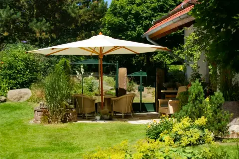 Terrasse mit Sonnenschirm und Sitzgruppe am Rand einer Rasenfläche