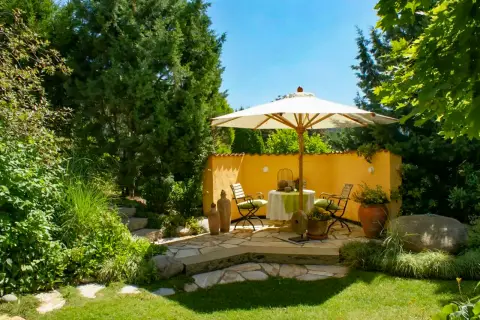 Sitzplatz mit Sonnenschirm unter Bäumen an einer Gartenmauer
