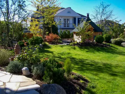 Garten mit Rasen, Staudenbeeten und hellem Gartenhaus im Hintergrund