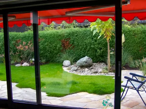 Blick durch eine Glastür auf einen Kiesgarten mit Findlingen