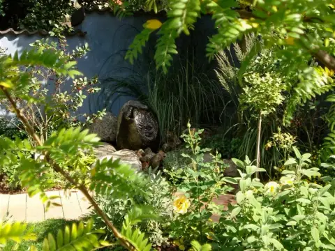 Steinfigur zwischen dichtem Blattwerk im Garten