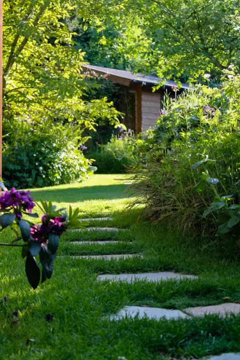 Trittsteinweg über eine Rasenfläche zwischen Beeten und Gartenhaus