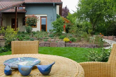 Gartentisch aus Geflecht mit blauen Vogel-Figuren, dahinter Rasen