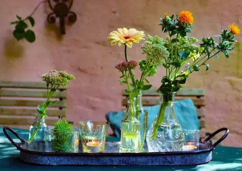 Tablett mit Blumenvasen und Kerzen auf einem Gartentisch