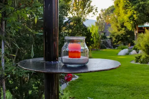 Kerze im Glas auf einem Metallständer, dahinter der Garten