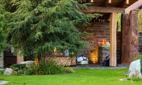 Steinerner Gartenunterstand mit Nadelbaum im Abendlicht