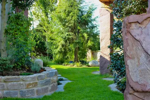 Garten mit Sandstein-Hochbeet, Nadelgehölzen und Pergola