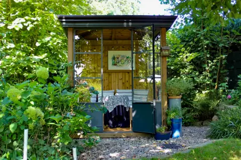 Gläsernes Gartenhaus mit Bildern, umgeben von Grün