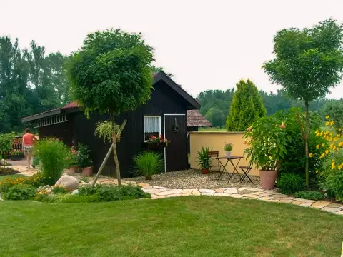 Dunkles Gartenhaus mit Bistro-Tisch am Rand einer Rasenfläche