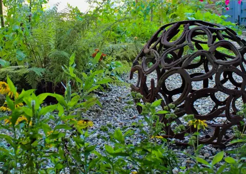 Kugelförmige Metallskulptur als Blickfang in einem Beet aus Gräsern und Stauden