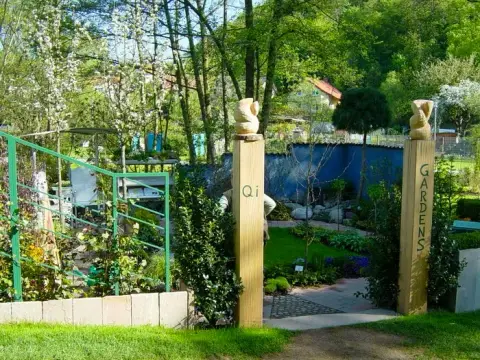 Blick durch das hölzerne, mit „Qi Gardens“ beschriftete Eingangstor auf den fertigen Schaugarten im Frühling