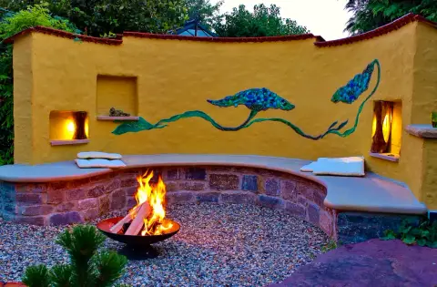 Fertiger Garten: geschwungene Gartenmauer mit Feuerschale und Sitznische am Abend