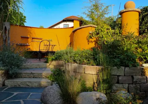 Fertiger Garten: terracottafarbene Mauer mit Stufen, Gräsern und Findlingen