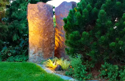 Fertiger Garten: angestrahlte Sandstein-Stele neben einer Kiefer