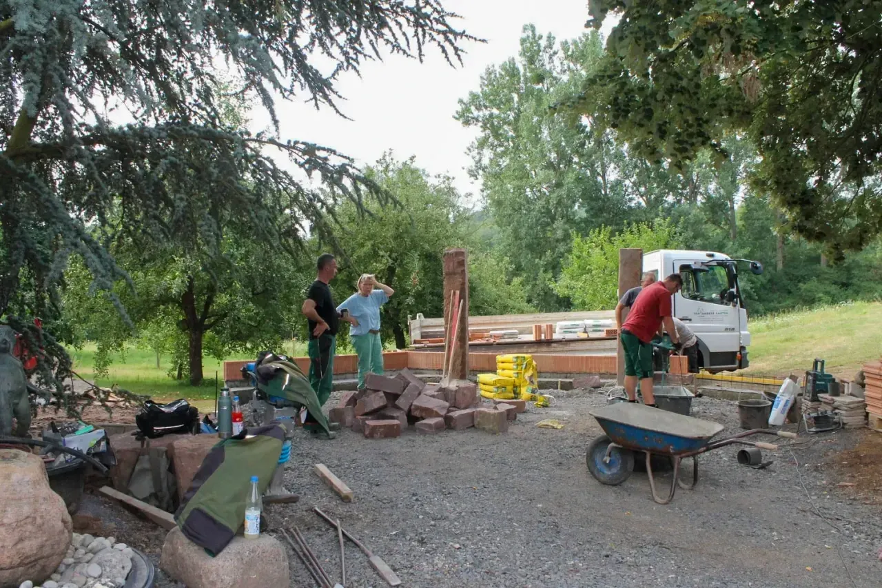 Bauphase auf der Gartenbaustelle: Natursteinarbeiten mit Sandsteinquadern, Schubkarre und Team bei der Umsetzung vor Ort