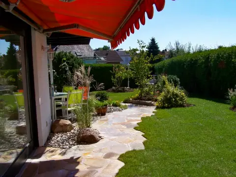 Ergebnis: gegliederter Gartenraum mit geschwungenem Natursteinweg, Gräsern und Sitzbereich unter Markise