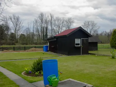 Ausgangslage: dunkles Gartenhaus an einer schlichten Rasenfläche